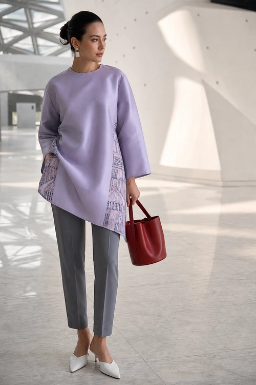 Lilac Tunic and Gray Trousers Outfit A woman wears a lilac asymmetrical tunic with patterned side panels, gray tapered trousers, white pointed shoes, and carries a burgundy handbag.