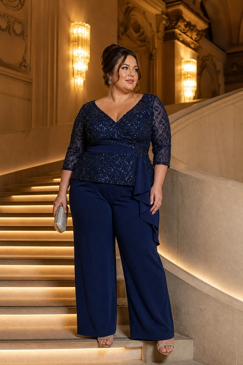 Navy Lace Top and Wide-Leg Trousers A woman wears a navy lace top with sheer three-quarter sleeves, wide-leg trousers, a draped waist detail, and carries a silver clutch on an illuminated staircase.
