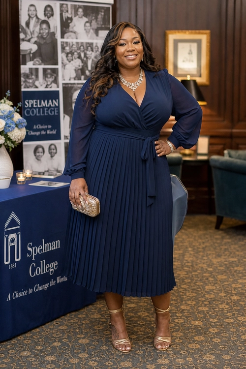 A woman wears a navy long-sleeve wrap dress with a pleated midi skirt, statement necklace, embellished clutch, and strappy metallic sandals.