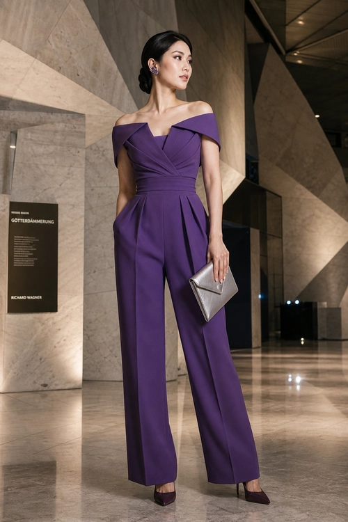 A woman wears a purple off-shoulder wide-leg jumpsuit with dark heels and carries a silver clutch.