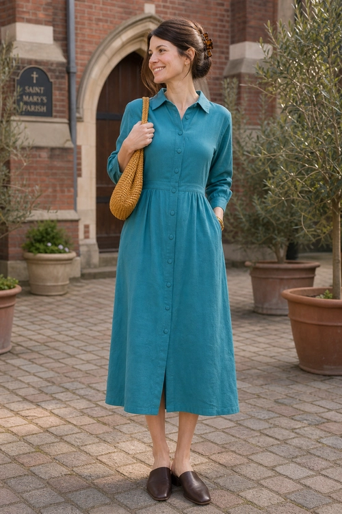A woman wearing a teal long-sleeve shirt dress with a woven mustard shoulder bag and brown slip-on loafers.