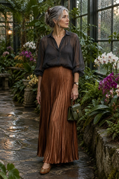 Black Blouse and Pleated Bronze Skirt A woman wears a sheer black button blouse with a bronze pleated maxi skirt, brown shoes, and an olive green handbag.