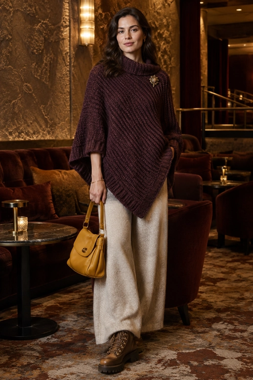 A burgundy oversized knit poncho with cream wide-leg trousers, brown lace-up boots, and a mustard leather handbag.