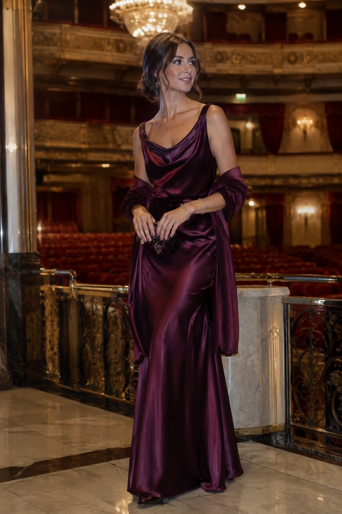 Plum Satin Evening Gown Woman wearing a plum satin cowl-neck gown with a matching draped shawl and beaded clutch.